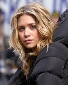 a woman with blonde hair and blue eyes wearing a puffy black jacket on the street