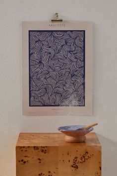 a bowl sitting on top of a wooden table next to a wall mounted art piece