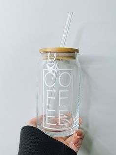 a person holding a glass jar with a straw in it that says coffee on the inside