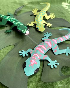 three geckos sitting on top of a sheet of green paper next to each other