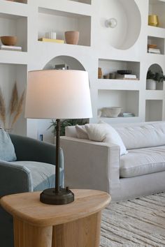 a living room filled with furniture and a lamp on top of a wooden table in front of a white wall