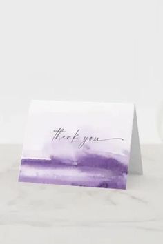 a purple and white thank card with the word thank you written in cursive ink