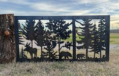 a metal sculpture with trees and animals in the grass next to a tree stump on a sunny day