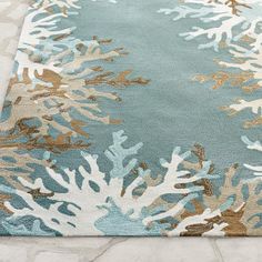 a blue rug with white and brown corals on it in front of a stone floor