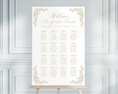 a white and gold wedding seating chart on an easel in front of a wall