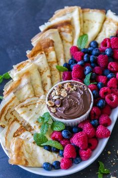 pancakes, raspberries and blueberries are arranged on a plate with chocolate sauce