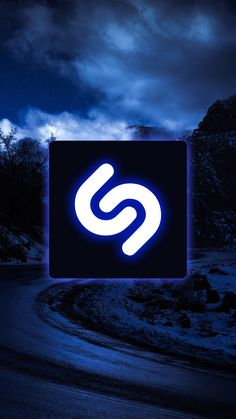 an illuminated sign on the side of a road at night with clouds in the background