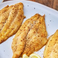 three fish fillets on a white plate with lemon wedges next to it and the words best baked catfish in dinner