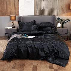 a bed with black sheets and pillows in a room next to a lamp on a table