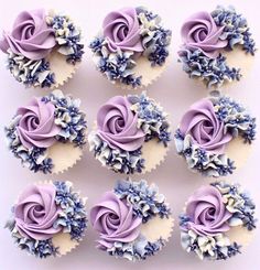 twelve cupcakes with purple frosting and blue flowers on them are arranged in rows