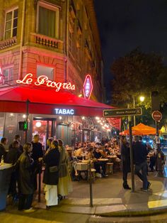 a group of people sitting at tables in front of a restaurant with red awnings