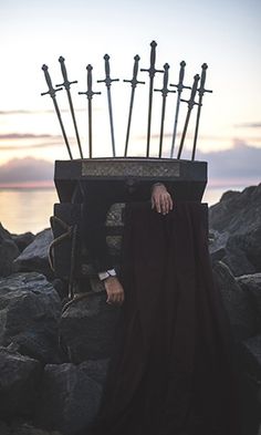 a man is sitting on some rocks with swords sticking out of his head in front of him