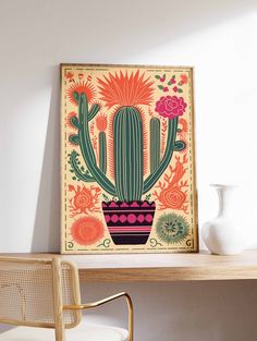 a cactus in a pot with flowers on the table next to a white vase and chair