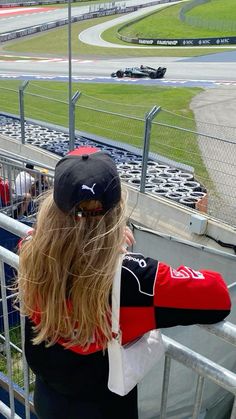 a woman standing on top of a metal fence next to a race track