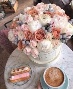 a cup of coffee sitting next to a pastry on top of a marble table covered in flowers