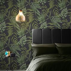 a bed with green leaves on the wall next to a night stand and side table