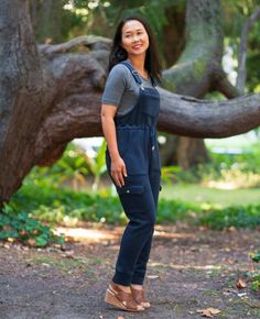 a woman standing in front of a tree with her hands on her hips and smiling at the camera