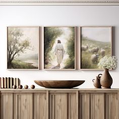 three paintings hang on the wall above a buffet with books and vases in front of it