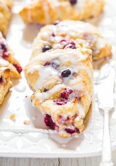 blueberry scones with icing on a white platter next to a fork