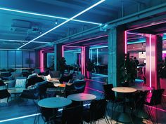 a room filled with lots of tables and chairs next to tall windows covered in neon lights