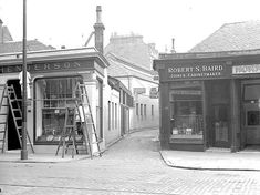 an old black and white photo of people in front of a barbershop with ladders on the sidewalk