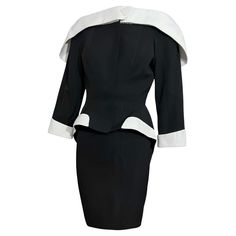 Own a piece of fashion history with this extraordinary documented Thierry Mugler Spring Summer 1996 skirt suit. Black and white jacket with a large folding collar and a large white statement button on the collar. Classic Mugler form with dramatic flared hips and slim waist. White trim at the hips and cuffs. Snap button closure. Comes with the matching black skirt. An identical suit is on display at the Thierry Mugler Couturissime exhibition, and one is also in the Chicago History Museums collection. Size: Both the jacket and skirt are a FR36 Condition: In excellent condition with little wear Jacket Measurements: Bust- 32" Waist- 24" Length- 25" Skirt Measurements: Waist- 24" Hips- 30" Length- 22" Givenchy Couture, Chicago History, Black And White Jacket, Artist Branding, Suit Black, Diana Ross, Thierry Mugler, Christian Lacroix, Harper's Bazaar