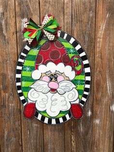 a christmas ornament hanging on the side of a wooden fence with a green and red santa clause