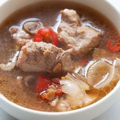 a white bowl filled with soup and meat on top of a table next to a spoon