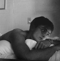 black and white photograph of a man in glasses laying on a bed with his arms crossed