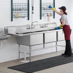 a woman cleaning a kitchen sink in front of two sinks with sprayers on the faucets