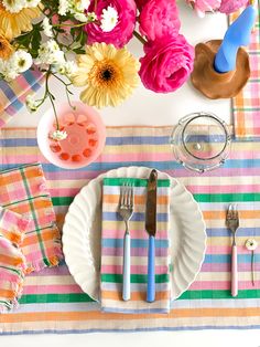 the table is set with colorful flowers, plates and utensils