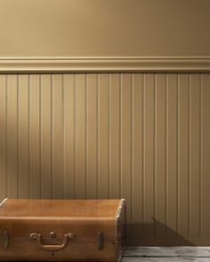 an old suitcase sitting on the floor in front of a wall with wood paneling