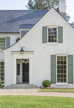 a white brick house with green shutters on the front door and windows in the side