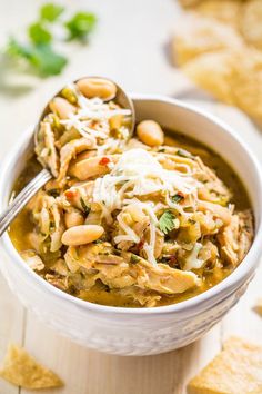 a white bowl filled with chicken and bean soup next to tortilla chips on the side