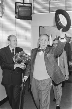 two men in suits and bow ties are walking through an office with flowers on the floor