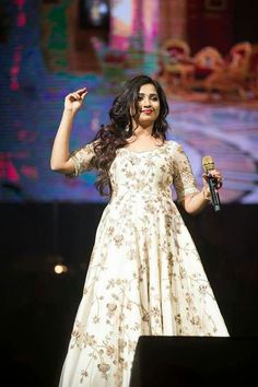 a woman standing on top of a stage with a microphone in her hand and wearing a white dress