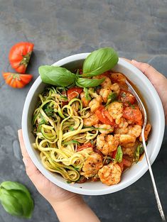 someone holding a bowl of shrimp and zucchini pasta