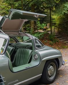 an old green car with its doors open and the hood up in front of it