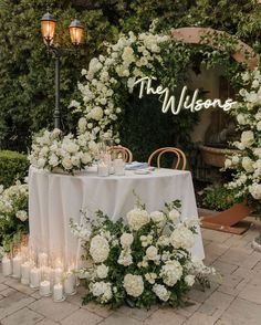 a table with white flowers and candles on it in front of a sign that says the wilsons