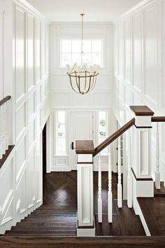 a white staircase with wood floors and chandelier