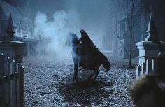 the dark knight is walking through the foggy street with his cloak draped over his head