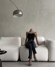 a woman sitting on top of a white couch in front of a wall mounted lamp