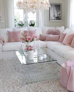 a living room with white couches, pink pillows and a chandelier hanging from the ceiling