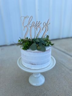 a white cake topped with greenery and a wooden class of 207 sign on top