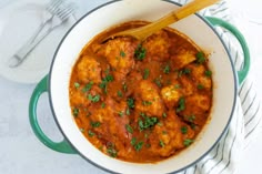 a pot filled with meatballs and sauce on top of a white table cloth next to a wooden spoon