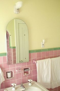 a bathroom with pink and green tiles on the walls, white towels hanging in front of a mirror