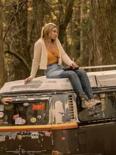 a woman is sitting on top of an old vehicle in the middle of the woods