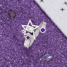 a silver ring with an amethorate and star on it sitting in front of purple glitter