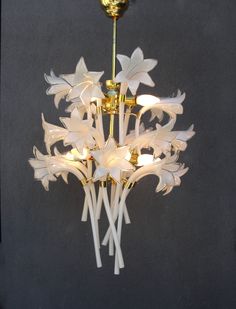 a chandelier with white flowers hanging from it's sides and gold accents