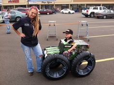 a woman standing next to a child in a toy truck made out of two large tires